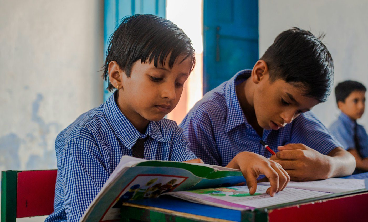 Two pupils reading a textbook together at their desk