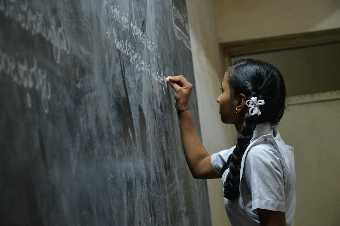 A student writing on the blackboard at the front of a classroom